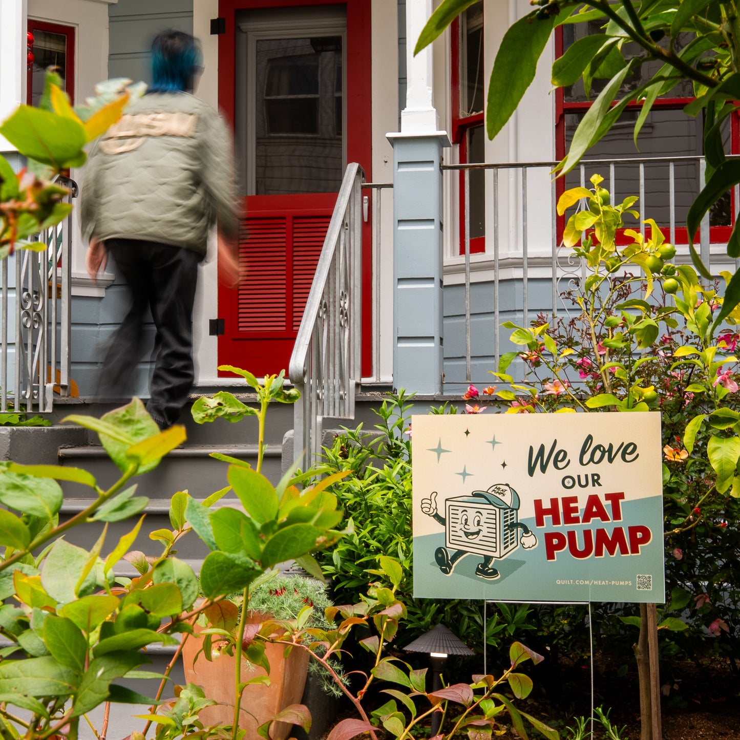 Person walking up a set of stairs to a house with a sign about love for a heat pump in the foreground.