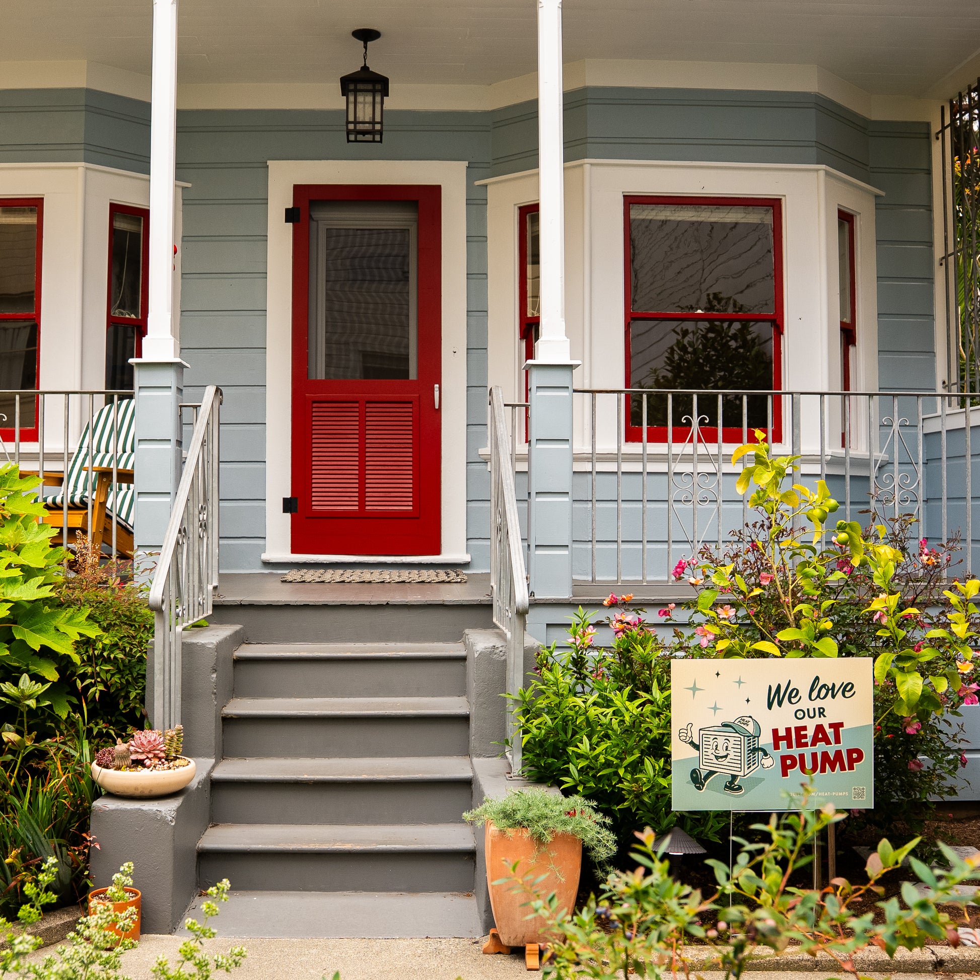 Front of a house with a red door and gray steps, featuring a 'We love our heat pump' sign.