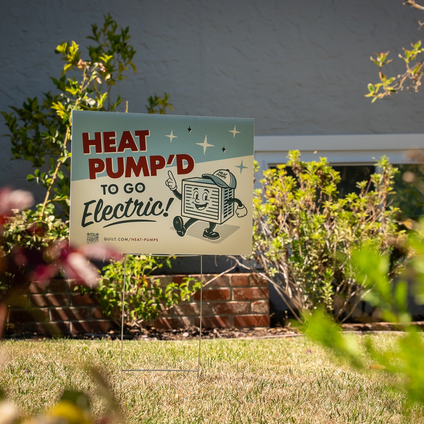 Garden sign with 'Heat Pump'd to go Electric!' text in a garden setting.