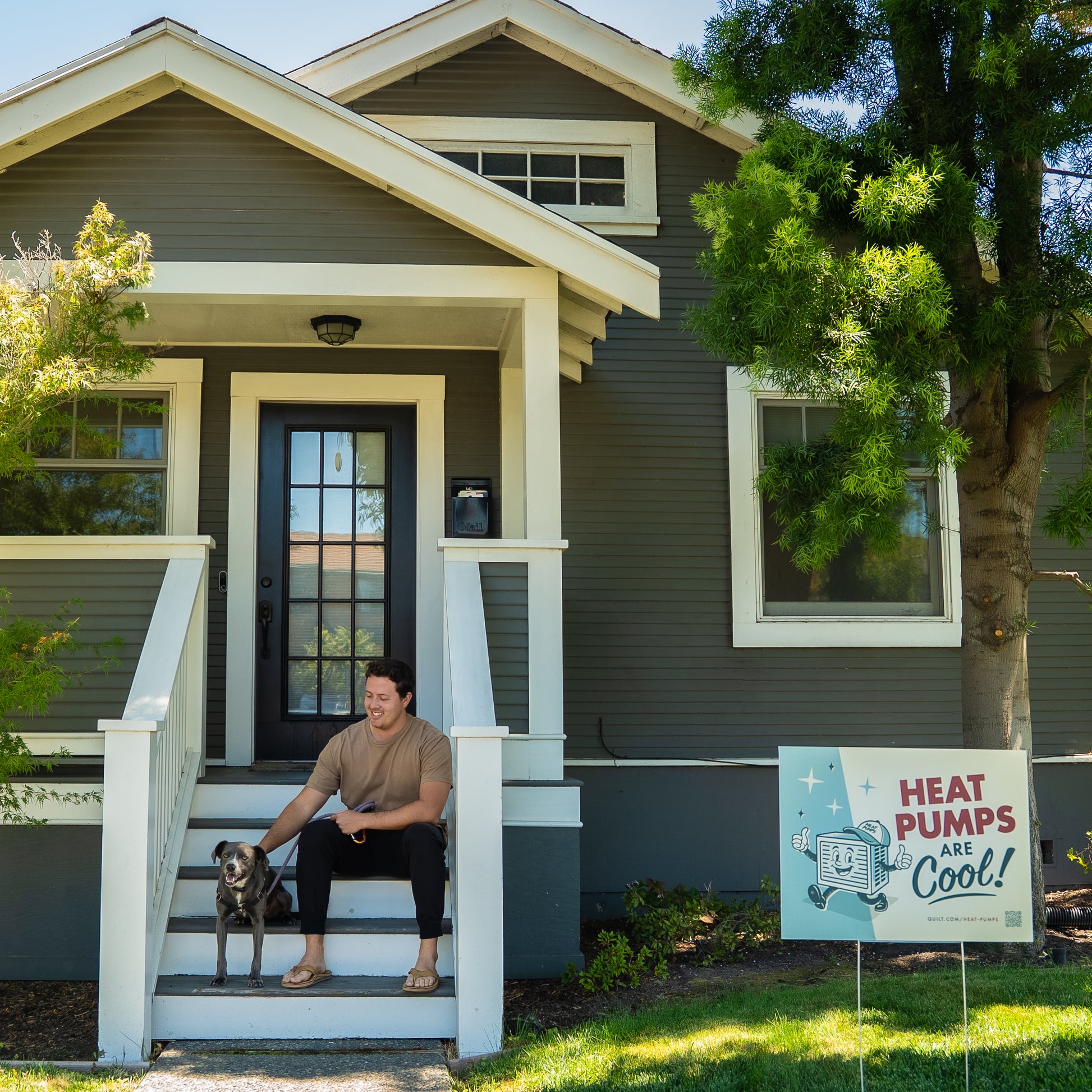 Person sitting on a porch with a dog, next to a 'Heat Pumps are Cool' sign in front of a house.